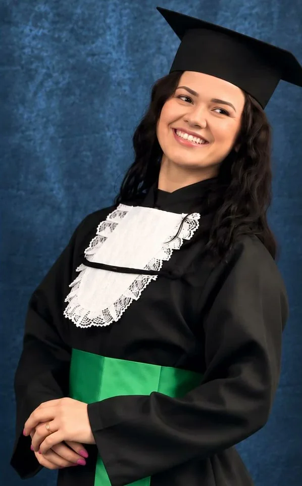 Gislaini Taiani sorrindo, de beca e capelo, na formatura em Nutrição
